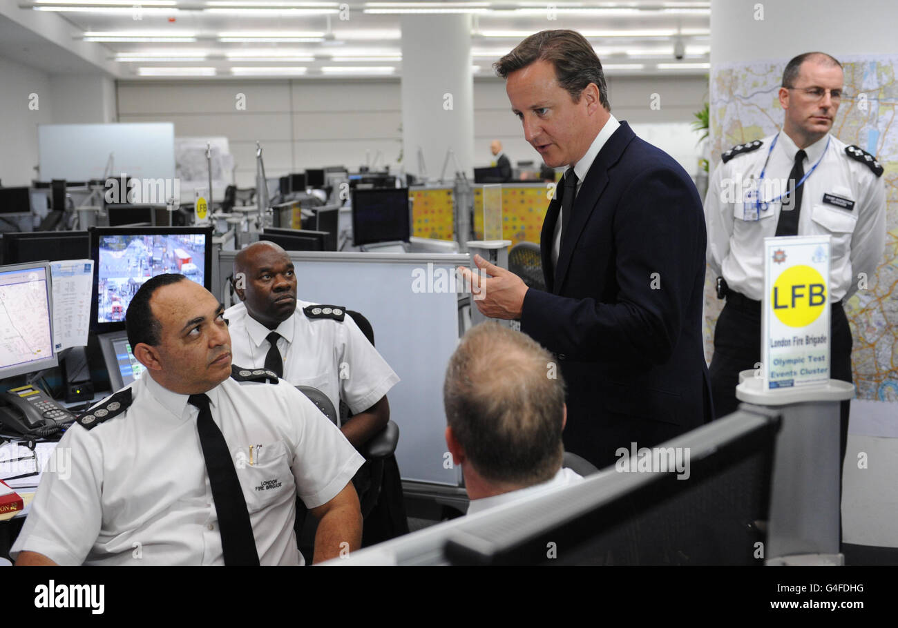 RITRASMISSIONE: Chiarire che gli ufficiali provengono dalla Brigata dei vigili del fuoco di Londra. Il primo ministro David Cameron parla con gli ufficiali (a sinistra) della Brigata dei vigili del fuoco di Londra durante una visita al quartier generale del comando dell'oro della polizia metropolitana a Lambeth, a sud di Londra, dopo aver tagliato la sua vacanza per prendere in carico la risposta del governo a tre giorni di disordini nella capitale e altrove. Foto Stock