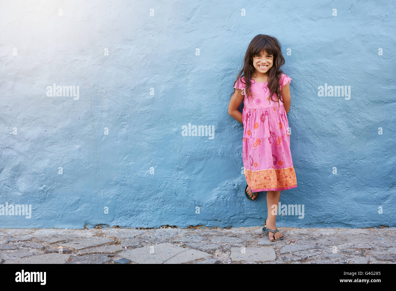 A piena lunghezza Ritratto di incantevole piccola ragazza sorridente mentre in piedi contro la parete blu con spazio di copia Foto Stock