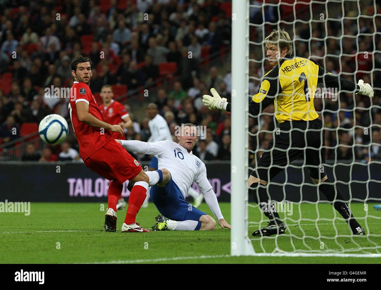 Wayne Rooney dell'Inghilterra guarda il suo tiro in grande come Joe Ledley del Galles (a sinistra) e Wayne Hennessey guardano (a destra) durante la partita di qualificazione UEFA Euro 2012 al Wembley Stadium di Londra. Foto Stock