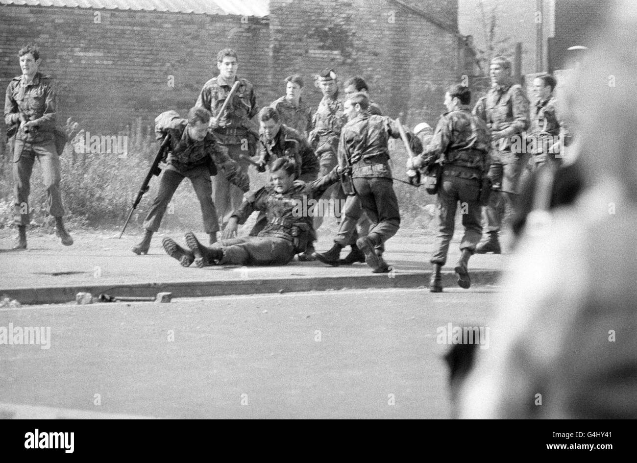 Un soldato ferito viene trascinato via dai suoi compagni durante una sommossa nella Falls Road, Belfast, il primo giorno della visita Silver Jubilee della Regina Elisabetta II in Irlanda del Nord. Foto Stock
