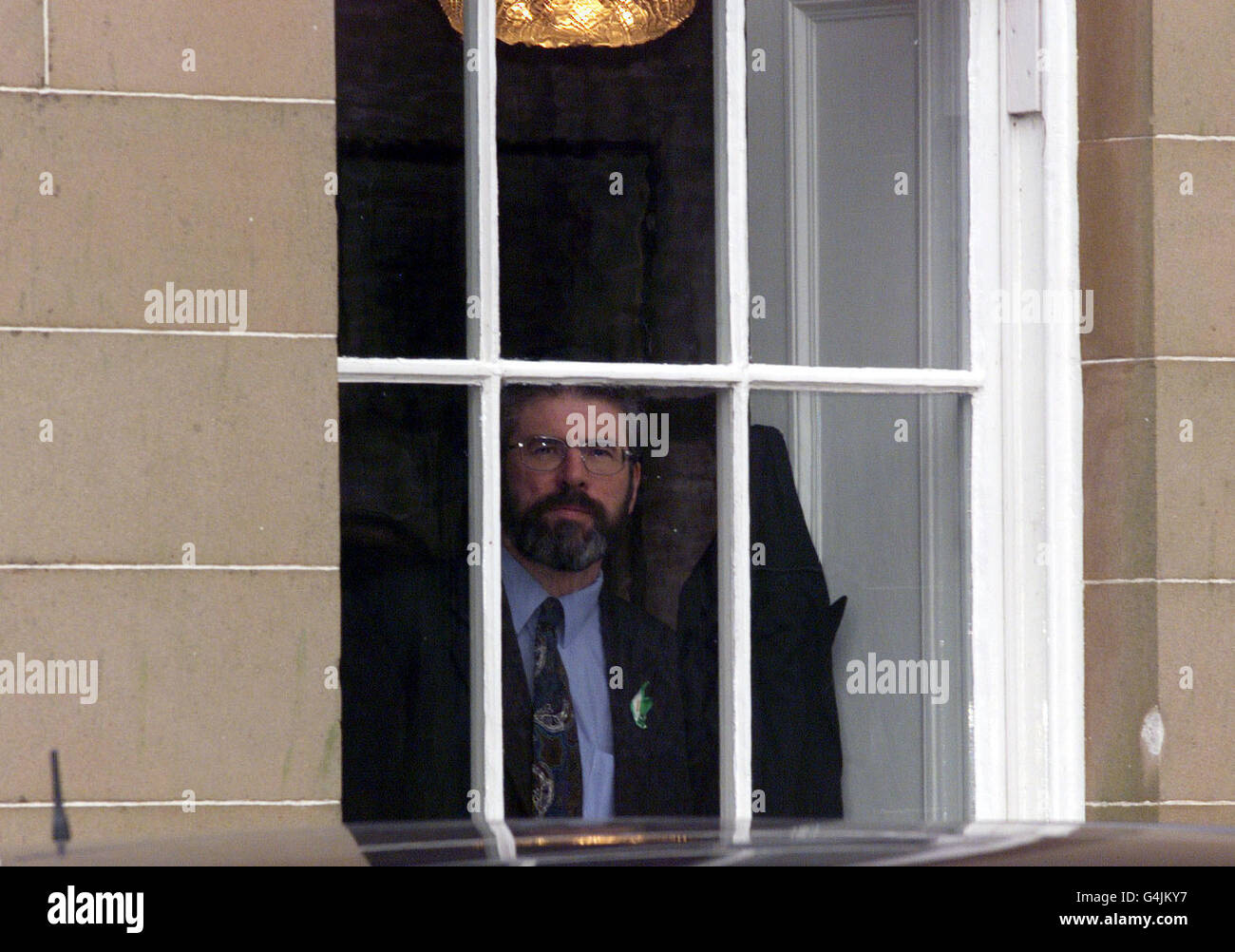 Il presidente del Sinn Fein Gerry Adams guarda dalla finestra al castello di Hillsborough. I vari partiti politici attendono che i primi ministri britannici e irlandesi tornino al castello per riprendere i colloqui. Foto Stock