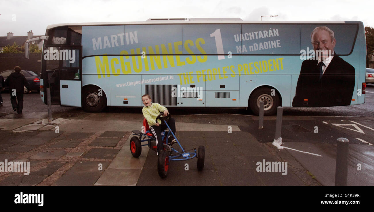 Un giovane su un go-kart pedala passando il candidato presidenziale Martin McGuinness 'campagna autobus durante la sua visita a Neilstown mentre si canvinava nella zona. Foto Stock