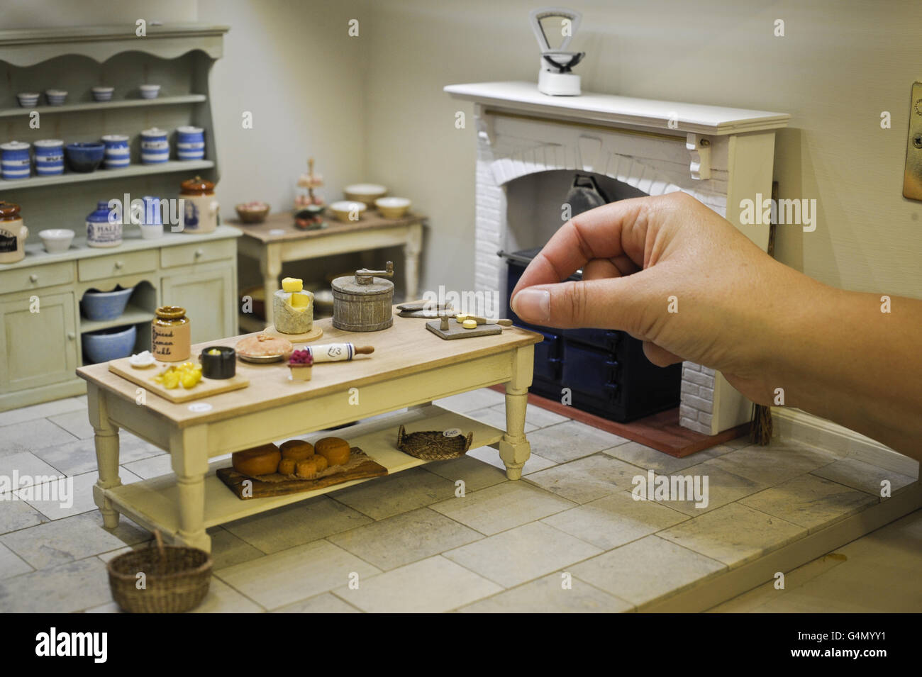 Le mani si raggiungono per un burro-pat in miniatura in una scena di cucina. PREMERE ASSOCIAZIONE foto. Data immagine: Giovedì 29 settembre 2011. Il negozio Karon Cunningham Miniatures di Bath, Regno Unito, offre una vasta e variegata collezione di mobili in miniatura, accessori e figurine realizzati da alcuni dei più importanti produttori di miniature del mondo. Il credito fotografico dovrebbe essere: Ben Birchall/PA Wire Foto Stock