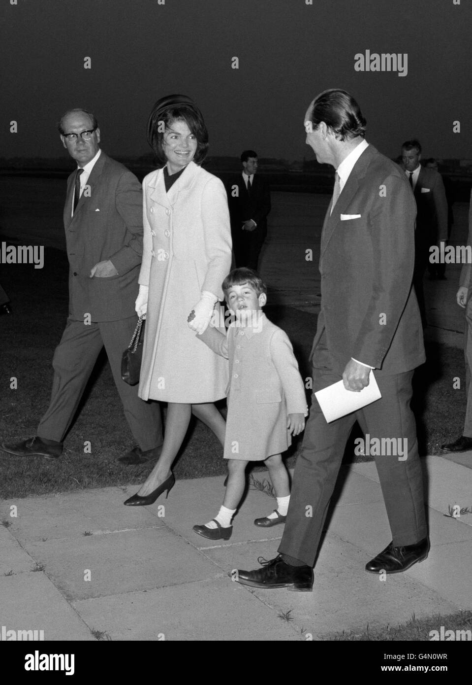 La signora Jackie Kennedy, tenendo la mano del figlio John Jr, sorride mentre cammina dall'aereo presidenziale degli Stati Uniti dopo l'atterraggio all'aeroporto di Londra. Ha volato sopra con i suoi due bambini per assistere alla scoperta da parte della regina di un memoriale al suo marito assassinato, il presidente John F Kennedy. Foto Stock