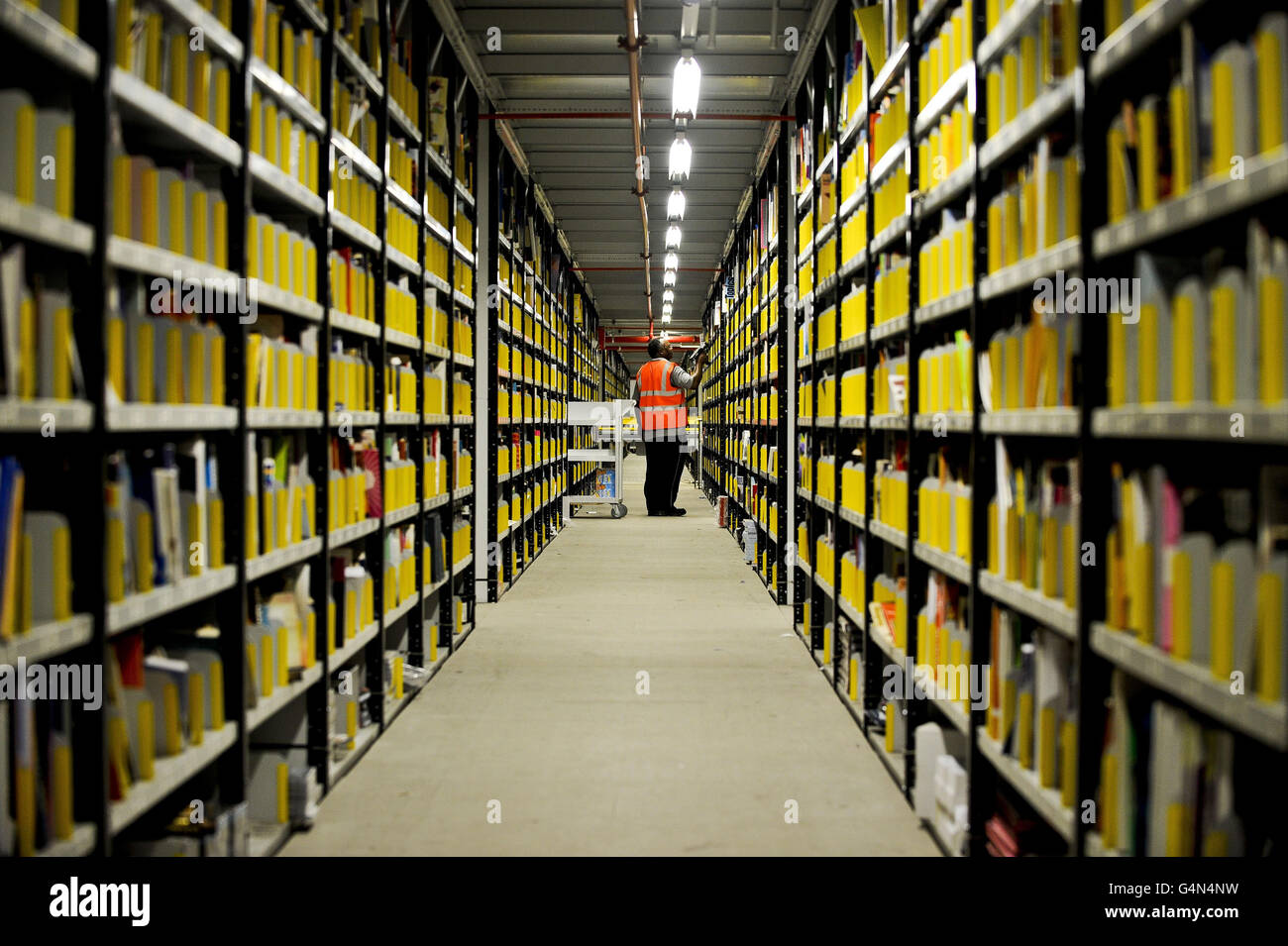 Un lavoratore presso il centro di adempimento Amazon a Swansea utilizza una pistola per la scansione di codici a barre per controllare e prelevare libri da un pavimento a un'area di scaffalatura del soffitto, di cui ci sono un numero sparso su una grande area nel centro. Foto Stock
