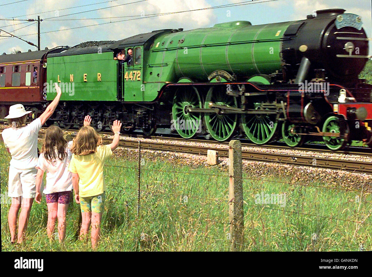 I bambini della ferrovia ondeggiano mentre la folla si trova tra York e Londra per osservare la velocità di Flying Scotsman lungo la East Coast Main Railway Line, tornando da una settimana in mostra al National Railway Museum di York. * 1/3/02: Più di 1,000 appassionati di treni hanno acquistato una quota nella locomotiva famosa in tutto il mondo, è emerso. Flying Scotsman plc ha aumentato 850,000 attraverso una quota che ha posto in anticipo rispetto alla sua flottazione sul mercato azionario il mese prossimo. Il collocamento chiuso ieri sera e la quantità di denaro raccolto fa sì che l'azienda abbia ora a disposizione 1.95 milioni di euro in più. Foto Stock