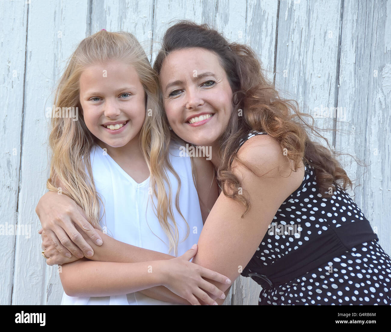 Sorridente madre caucasica abbracciando piccola bionda figlia dal vecchio fienile dipinte di bianco. Foto Stock