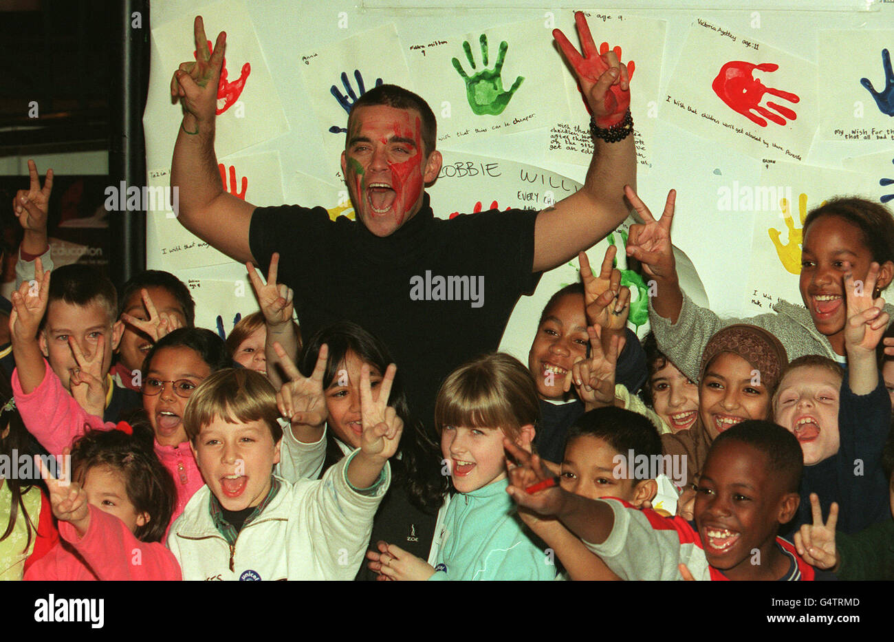 Robbie Williams con i bambini della Torriano Junior School a Kentish Town, East London, ha fatto il suo segno per una campagna Unicef a East London. Il cantante, ha aggiunto le sue stampe a una mostra per segnare 10 anni della convenzione delle Nazioni Unite sui diritti dei bambini. Foto Stock