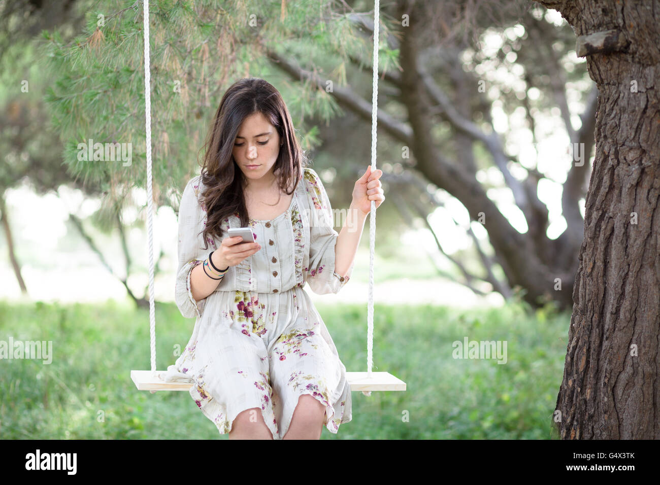 Donna con lo smartphone su un altalena in un parco Foto Stock