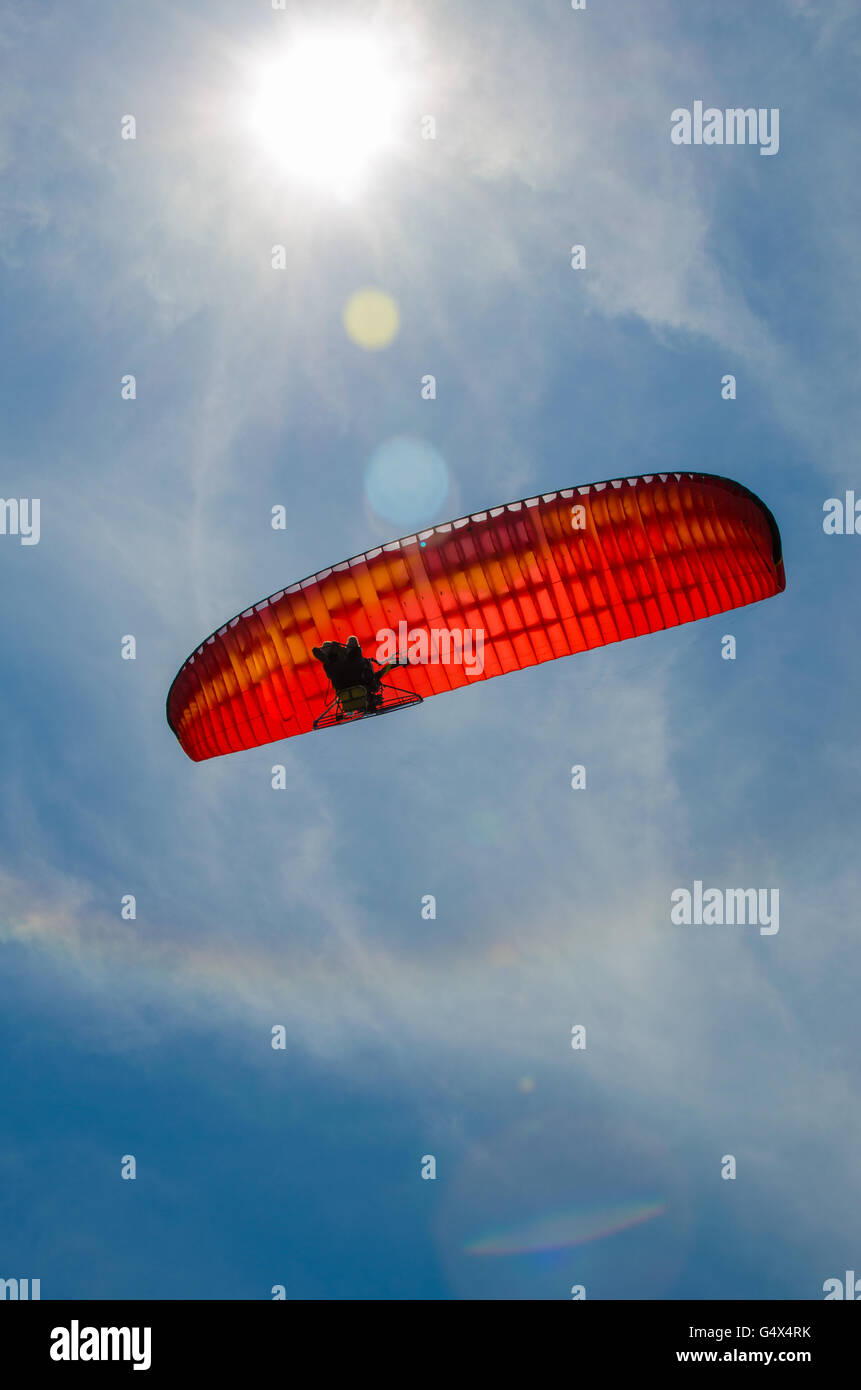 Basso angolo di visione della persona parapendio motore contro un cielo azzurro e sole splendente con lens flare Foto Stock