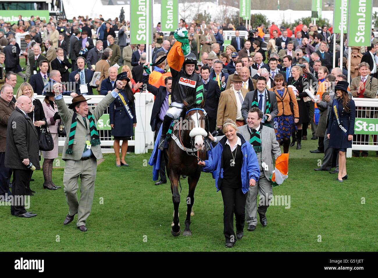 Cinders e Ashes guidati dal fantino Jason Maguire sono condotti nella recinzione dei vincitori insieme ai proprietari Phil Cunningham (davanti, a destra) e Dermot Hanafin (davanti, a sinistra) dopo aver vinto l'hurdle dei novizi supremi di William Hill il Centenary Day, durante il Cheltenham Festival. Foto Stock