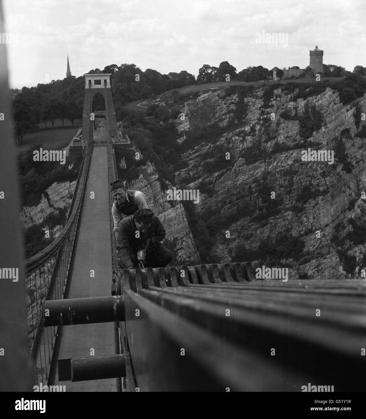 Questo non è un lavoro per gli uomini che ottengono incantesimi ridenti, ma Gilbert Taylor (più vicino) e Alfred Stadon sono ormai ben abituati ad alture. Sono gli uomini di manutenzione residenti con il lavoro a tempo pieno di cura del famoso Clifton Suspension Bridge sopra il Portway a Bristol. Sono visti al lavoro con le loro lattine di olio sulle 'catene' in alto sopra la carreggiata. Foto Stock