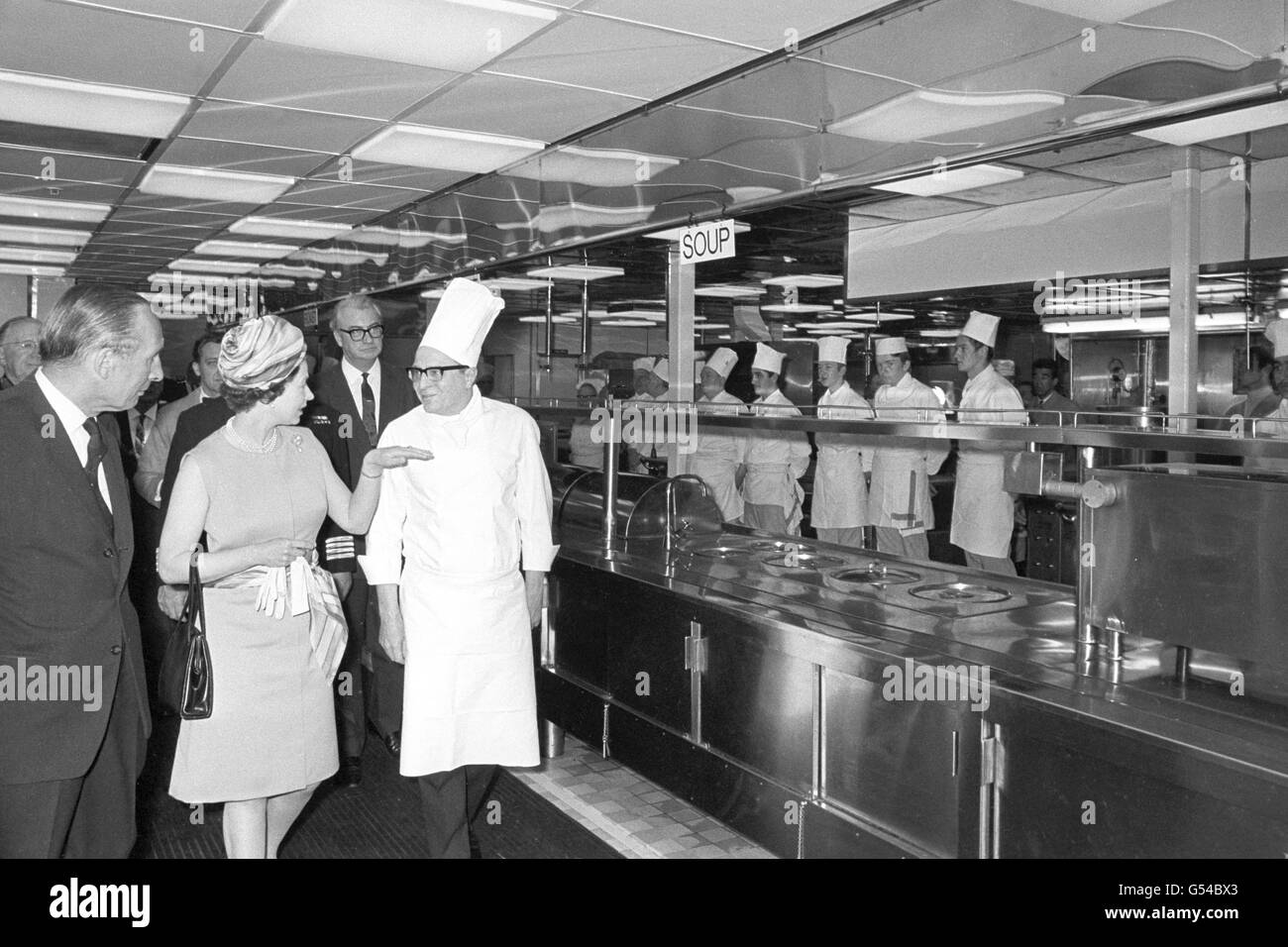 La regina Elisabetta II si interroga con uno degli esperti mentre visita le cucine durante la sua visita al QE2 a Southampton, alla vigilia del primo viaggio transatlantico a New York. Foto Stock