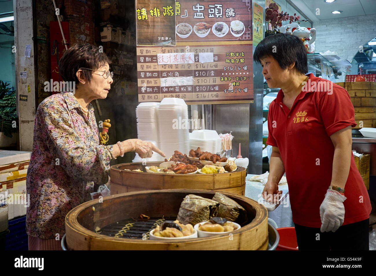 Titolare di una pensione o di una rendita ricorda ed interroga il prezzo di alcuni siu mai a un fornitore in stallo su Chun Yeung Street, Northpoint, Hong Kong. Foto Stock