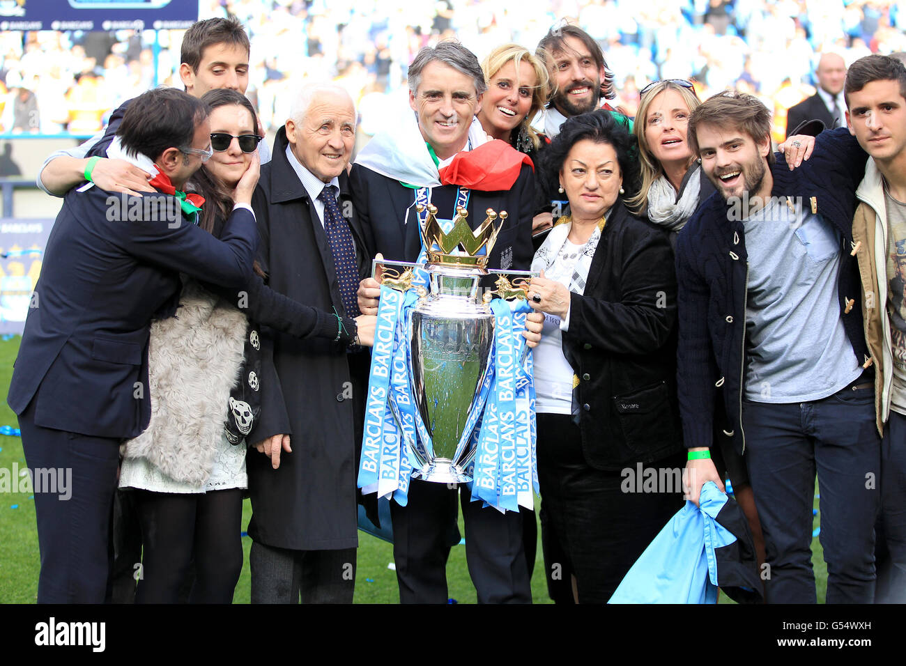Il manager della città di Manchester Roberto Mancini (al centro), drappeggiato in una Bandiera Italiana, festeggia insieme al padre Aldo (4° a sinistra), alla moglie Federica (6° a destra) e alla madre Marianna (4° a destra) con il Barclays Premier League Trophy Foto Stock