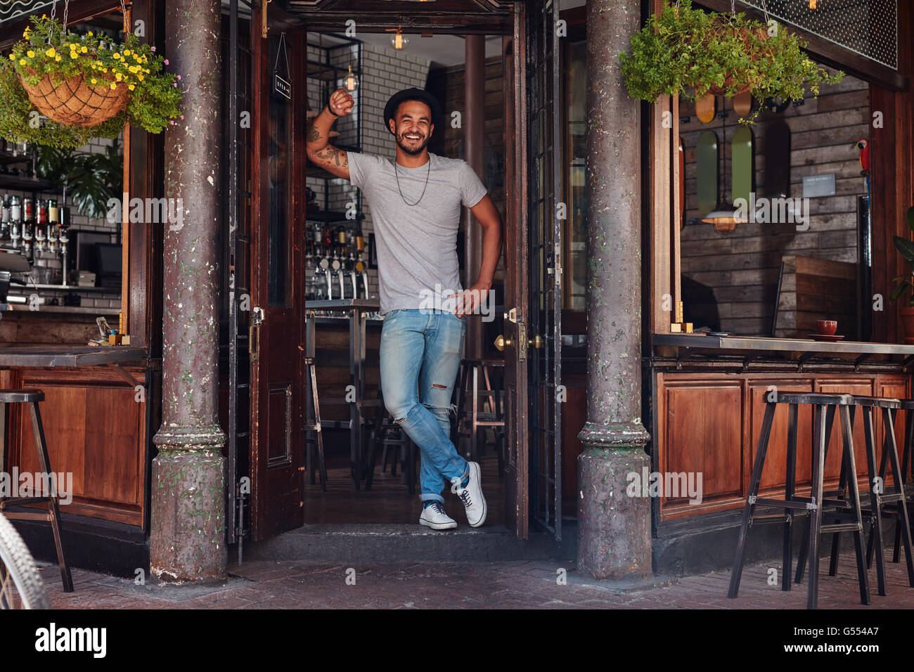 A piena lunghezza Ritratto di giovane sorridente uomo in piedi alla porta di un cafe'. Rilassata giovane uomo moderno in un bar. Foto Stock