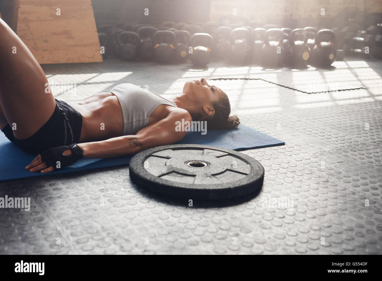 donna in forma fisica che si rilassa dopo l'allenamento in palestra. Piatto pesante sul pavimento con donna muscolosa sdraiata sul tappetino per esercizi. Foto Stock