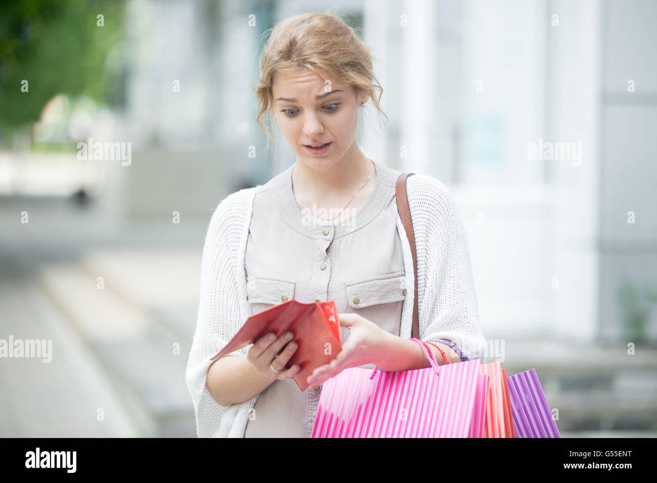 Ritratto di scontento ha sottolineato persona bella cercando in open wallet con espressione sconvolta mentre si tiene il colore delle borse per lo shopping Foto Stock