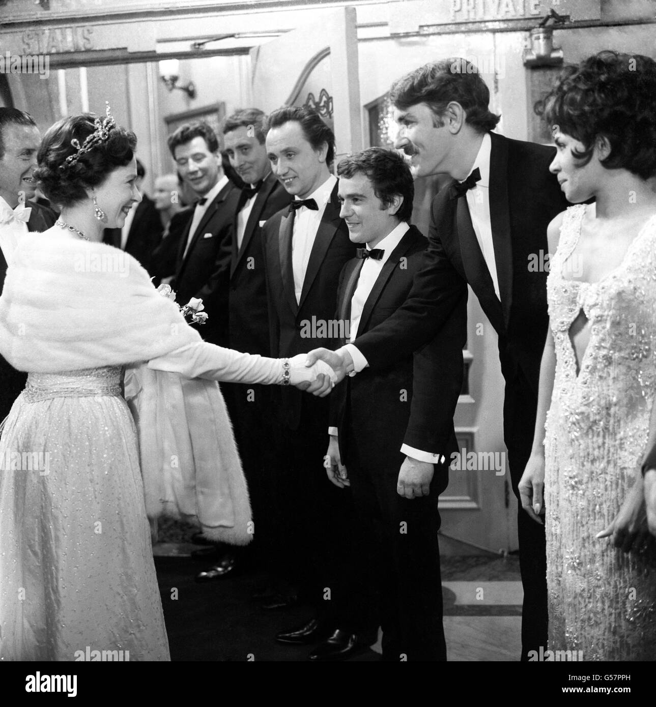 La regina scuote le mani con la star Peter Cook, non solo... ma anche, quando le stelle sono state presentate al Royal Variety Performance al London Palladium. La minutiva co-star di Cook, Dudley Moore, può essere vista a destra di Cook. Foto Stock
