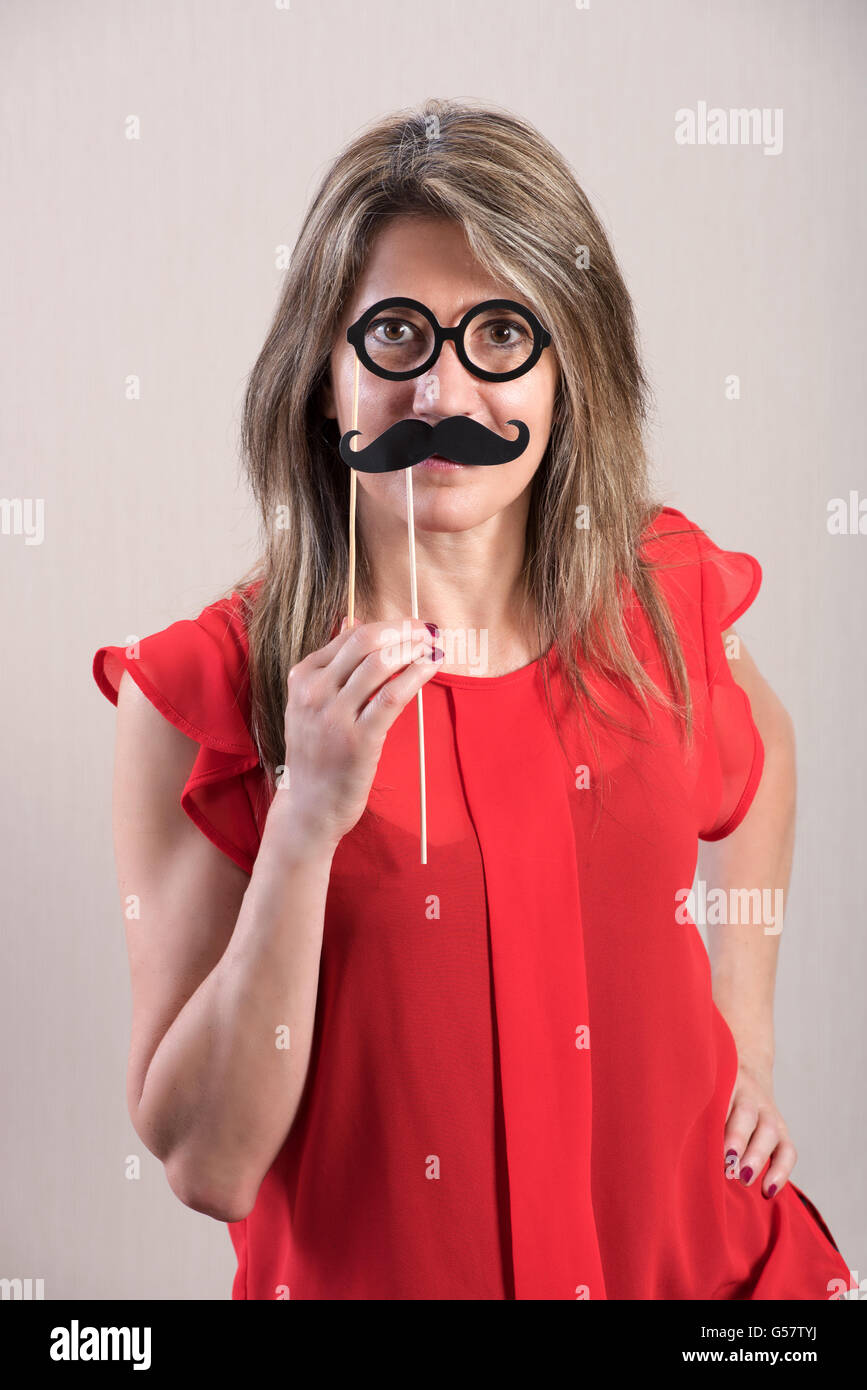 Mezzo Corpo colpo di una donna attraente Holding divertente i baffi e occhiali Photo Booth puntelli e guardare dritto verso la fotocamera. Foto Stock