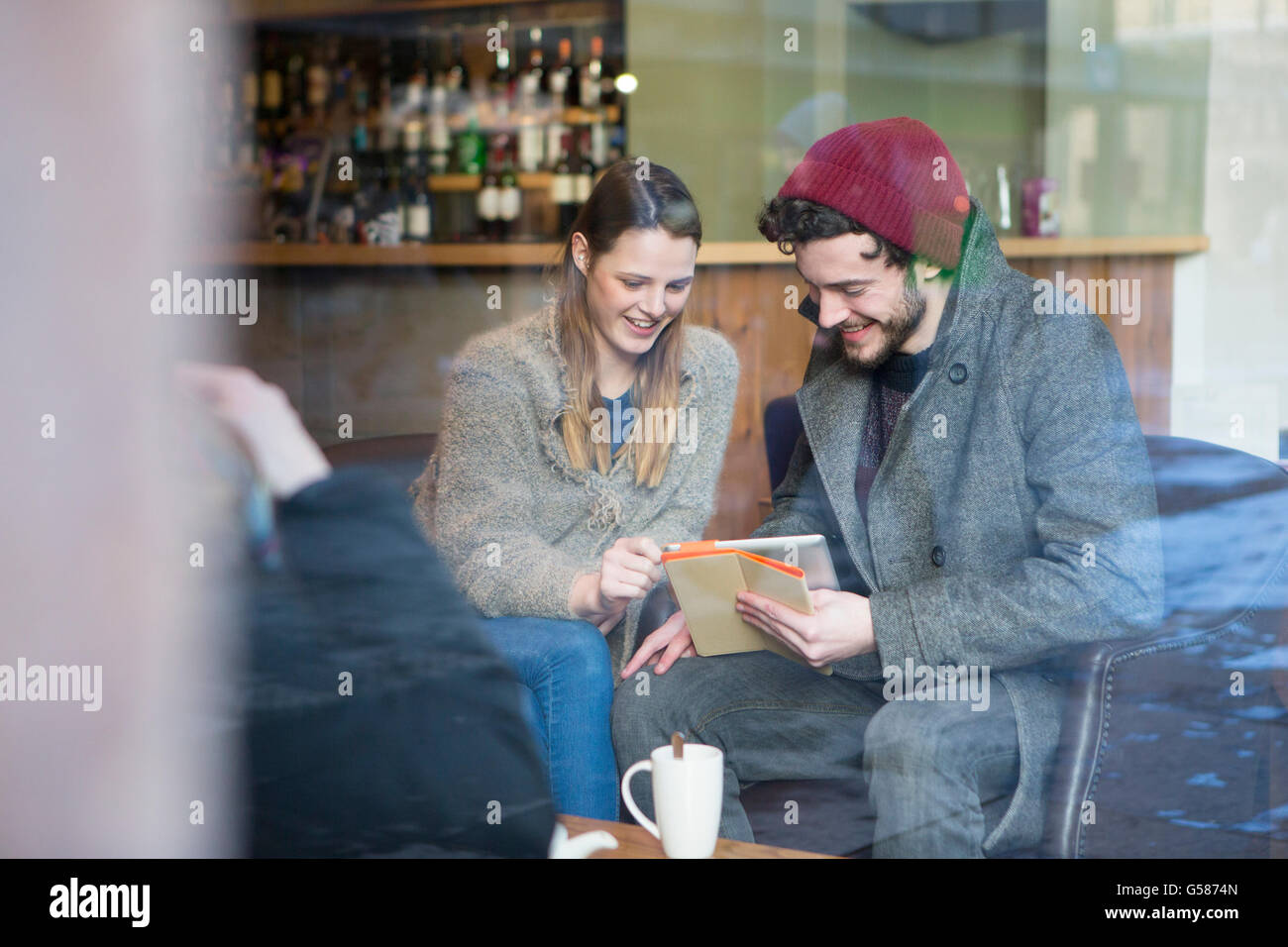 Giovane uomo e donna seduta in una caffetteria guardando una tavoletta digitale insieme. Foto Stock