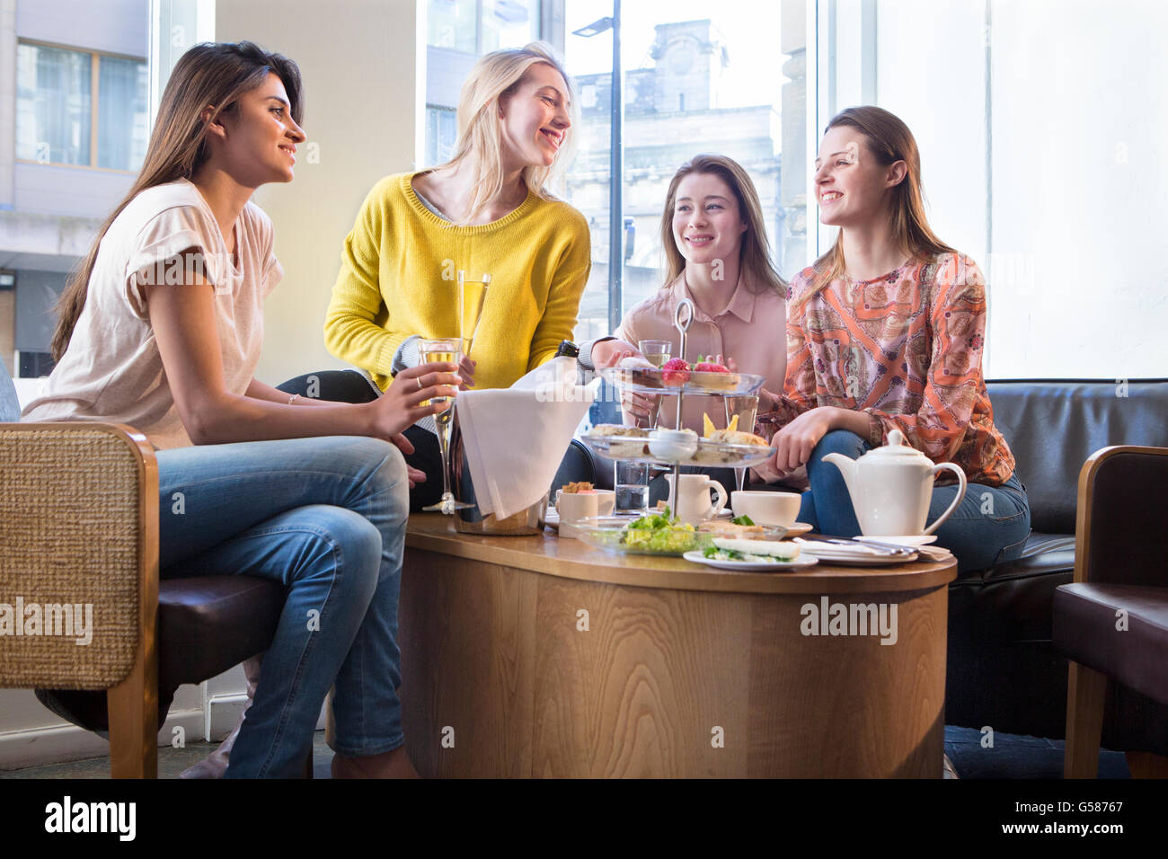 Quattro giovani donne seduti in un caffè e parlano tra loro oltre il tè del pomeriggio. Foto Stock