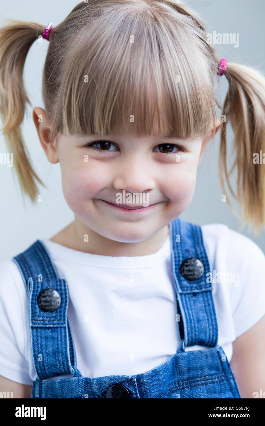 Carino giovane ragazza in salopette da sorridere alla telecamera Foto Stock