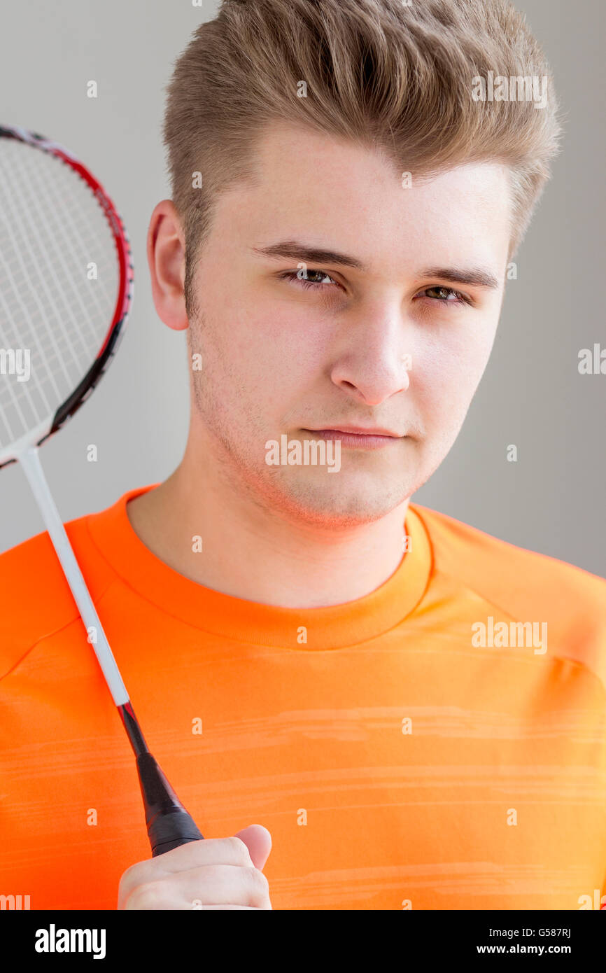 Ritratto di un ragazzo adolescente. Egli è in possesso di un campo di badminton racchetta e in piedi contro uno sfondo semplice Foto Stock