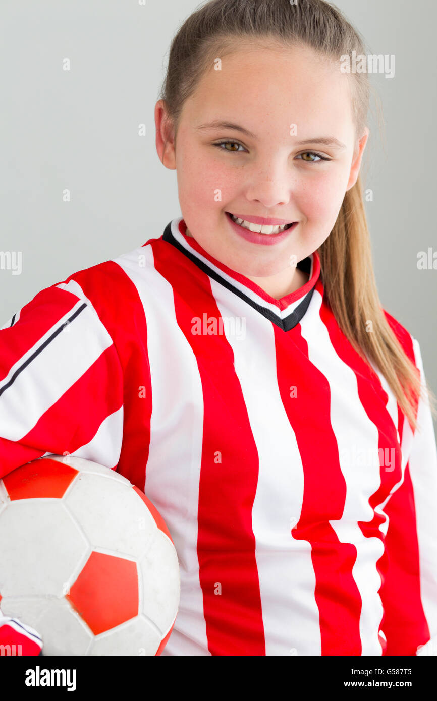 Femmina giocatore di calcio posa per la fotocamera con un calcio e il suo kit. Ella è contro uno sfondo semplice. Foto Stock