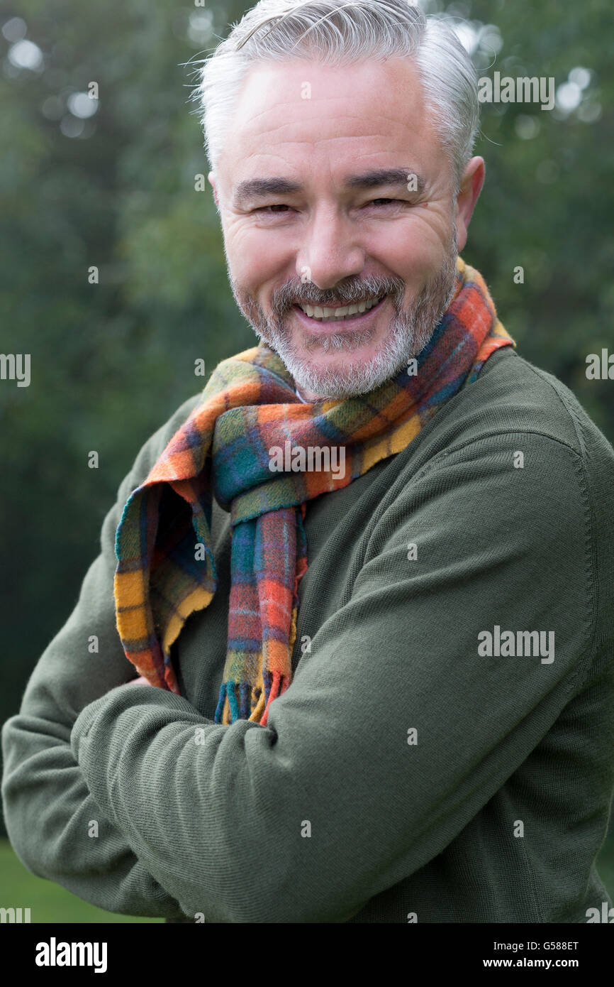Ritratto di un uomo con le braccia incrociate, sorridere per la fotocamera. Egli è al di fuori e gli alberi possono essere visti sullo sfondo. Foto Stock