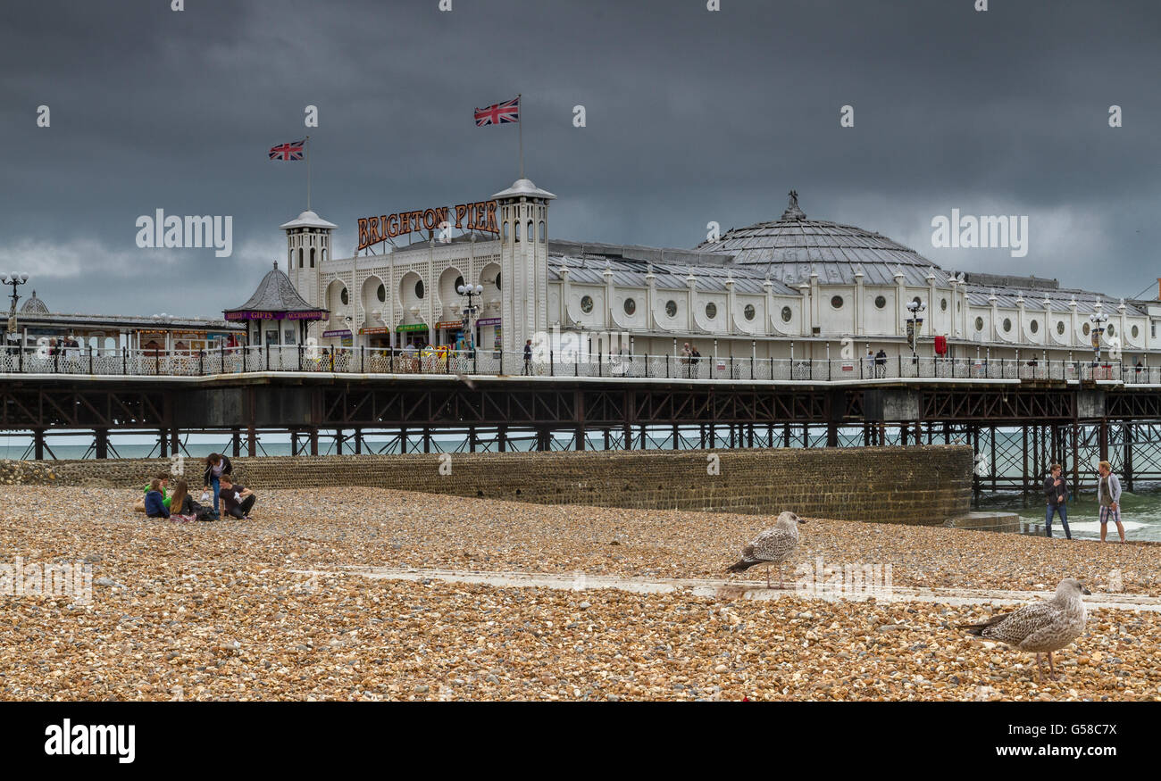 La gente seduta sulla spiaggia di Brighton in inverno, nei pressi di grado11 elencati Brighton Pier e Brighton Seafront , East Sussex, Regno Unito Foto Stock