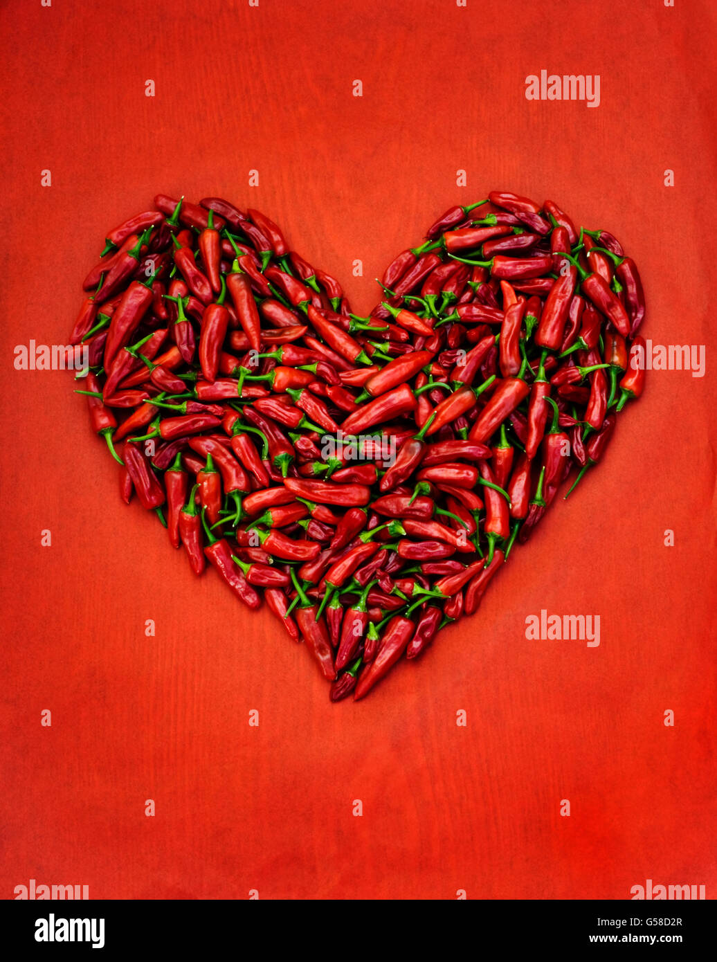 Peperoncino rosso cialde a forma di cuore sul tessuto rosso e la tavola di legno Foto Stock