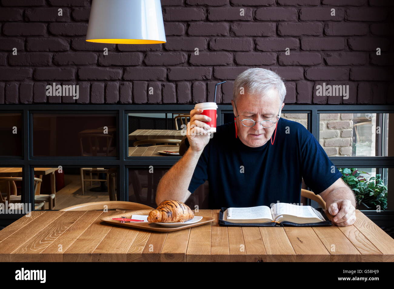 Uomo seduto a un tavolo con un caffè e un cornetto in uno snack bar e la lettura della Bibbia. Pausa di lavoro dedicato a quella spirituale Foto Stock