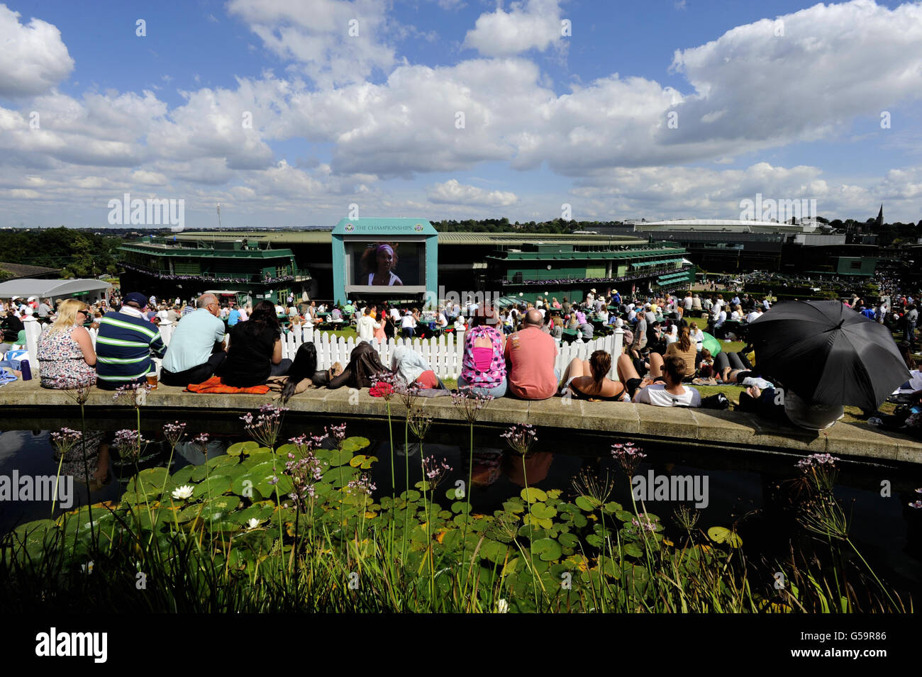 Gli appassionati di tennis godono del sole mentre guardano il grande schermo sul Monte Murray durante il giorno dieci dei campionati di Wimbledon 2012 all'All England Lawn Tennis Club, Wimbledon. Foto Stock