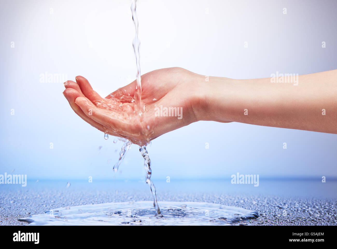L'acqua che cade in mano womans su bianco e lo sfondo blu Foto Stock
