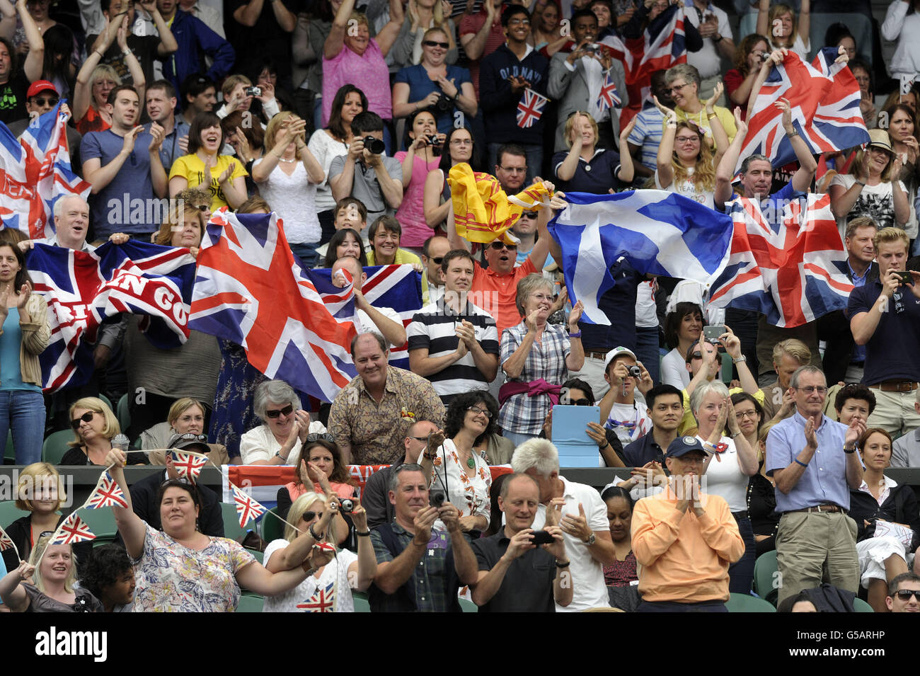 La folla si leverà in piedi e applaudì mentre Andy Murray della Gran Bretagna celebra la vittoria del suo primo round match nel Men's Singles al locale di tennis olimpico, Wimbledon. Foto Stock