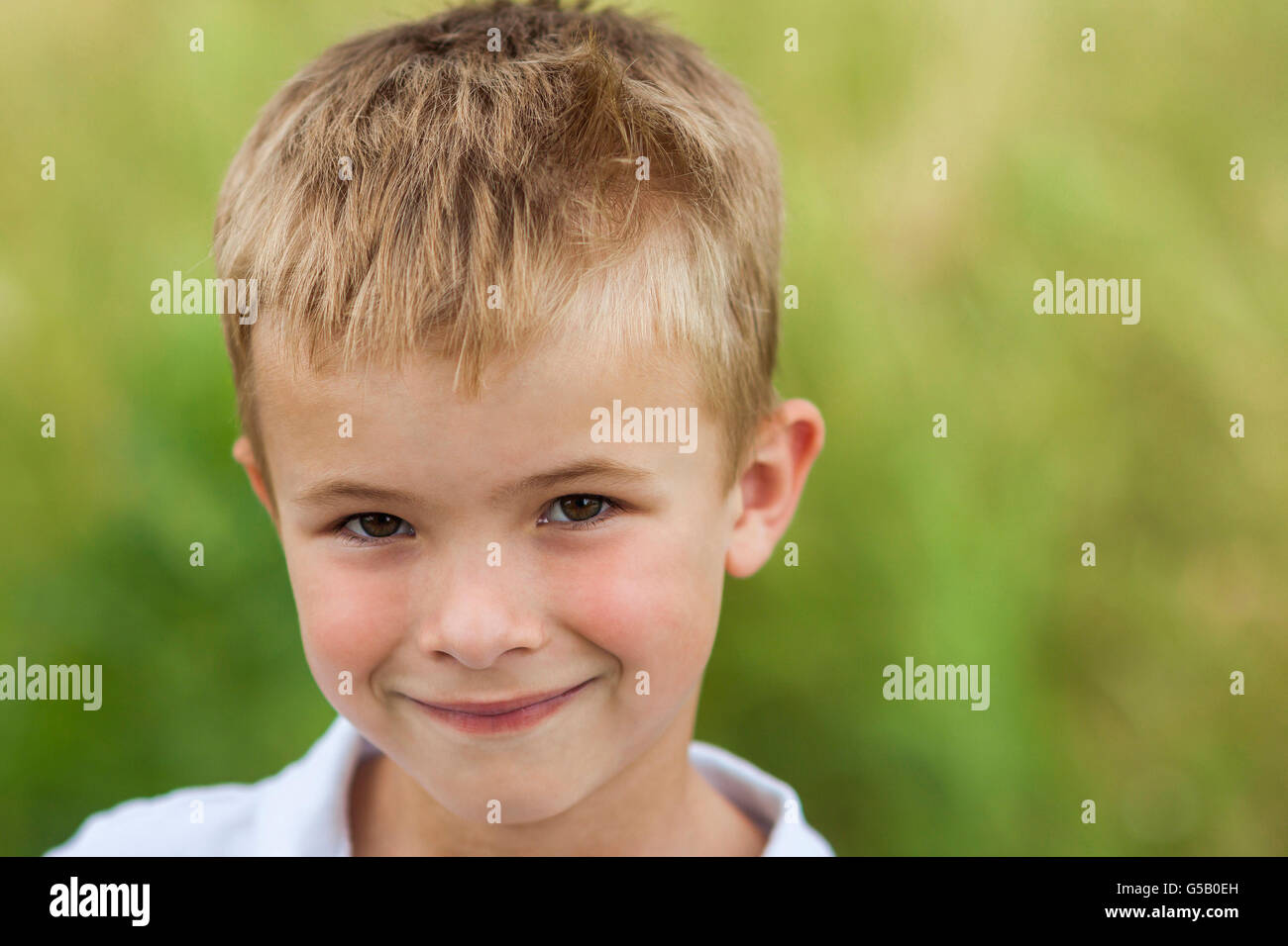 Ritratto di un piccolo ragazzo sorridente con la bionda dorata capelli di paglia nella soleggiata giornata estiva sul verde sfondo sfocato Foto Stock