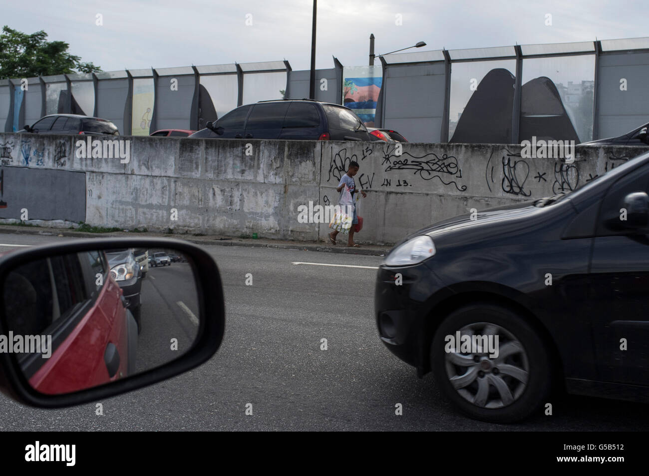 Il lavoro minorile, street venditore lavora durante le ore di punta di traffico a Linha Vermelha expressway ( Linea Rossa ), il principale collegamento tra il Rio de Janeiro / Antonio Carlos Jobim International Airport e la città, Brasile - opache in plastica dura e la divisione tra la strada e la Favela da mare, zona dominata dal traffico di stupefacenti. Foto Stock