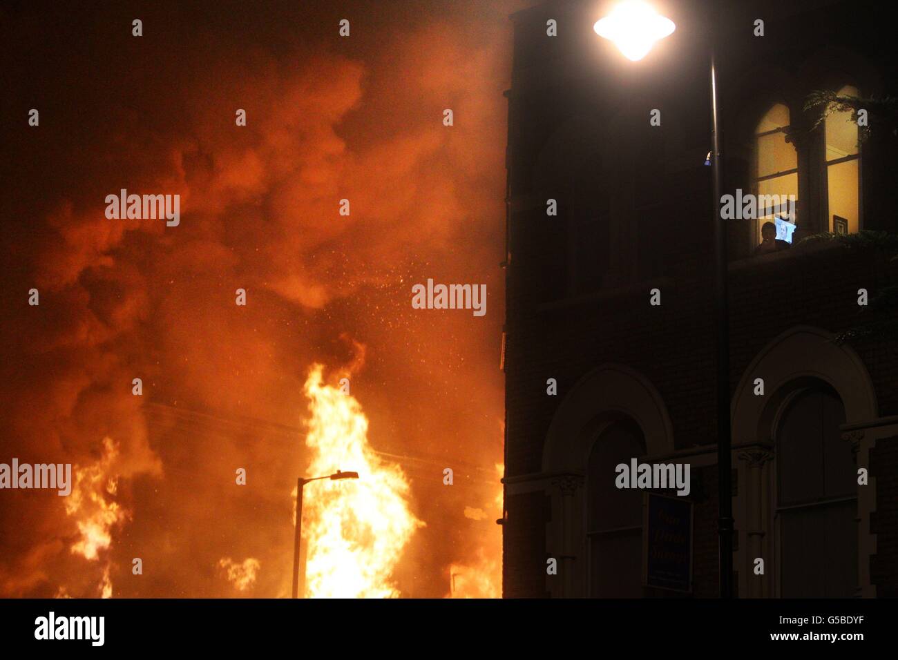 Foto inedita datata 07/08/11 dei tumulti estivi. Un uomo guarda fuori dalla sua finestra su Tottenham High Street come fiamme ingolfano l'edificio accanto, la sua televisione mostra una trasmissione della polizia circa la rivolta. Foto Stock