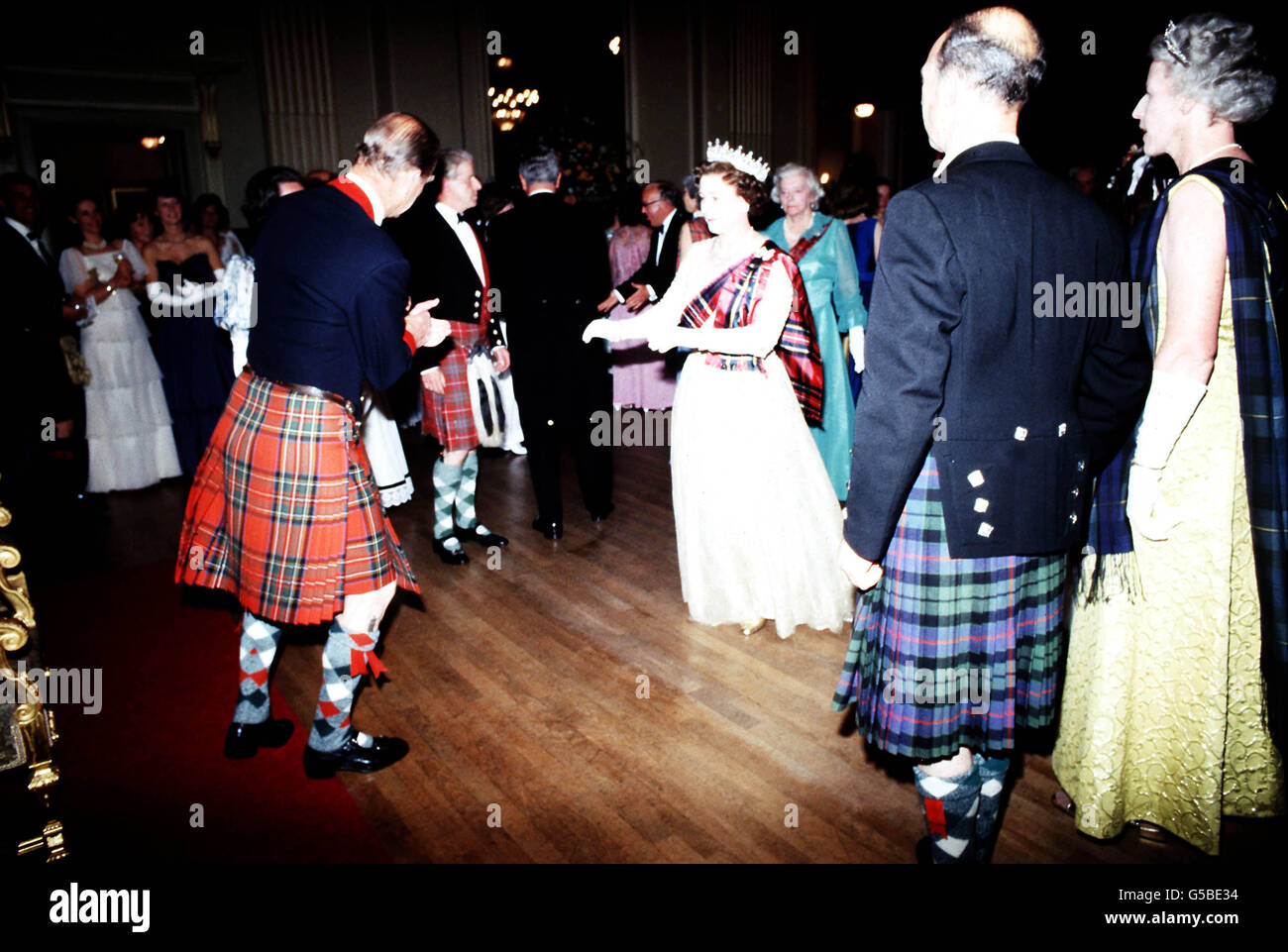 La regina Elisabetta II, in abito bianco e sash tartan, prende il pavimento con il duca di Edimburgo, in kilt, durante il Centenario della Società dei Piper Scozzesi nella Sala dell'Assemblea di Edimburgo, durante la loro visita di 7 giorni in Scozia. Foto Stock