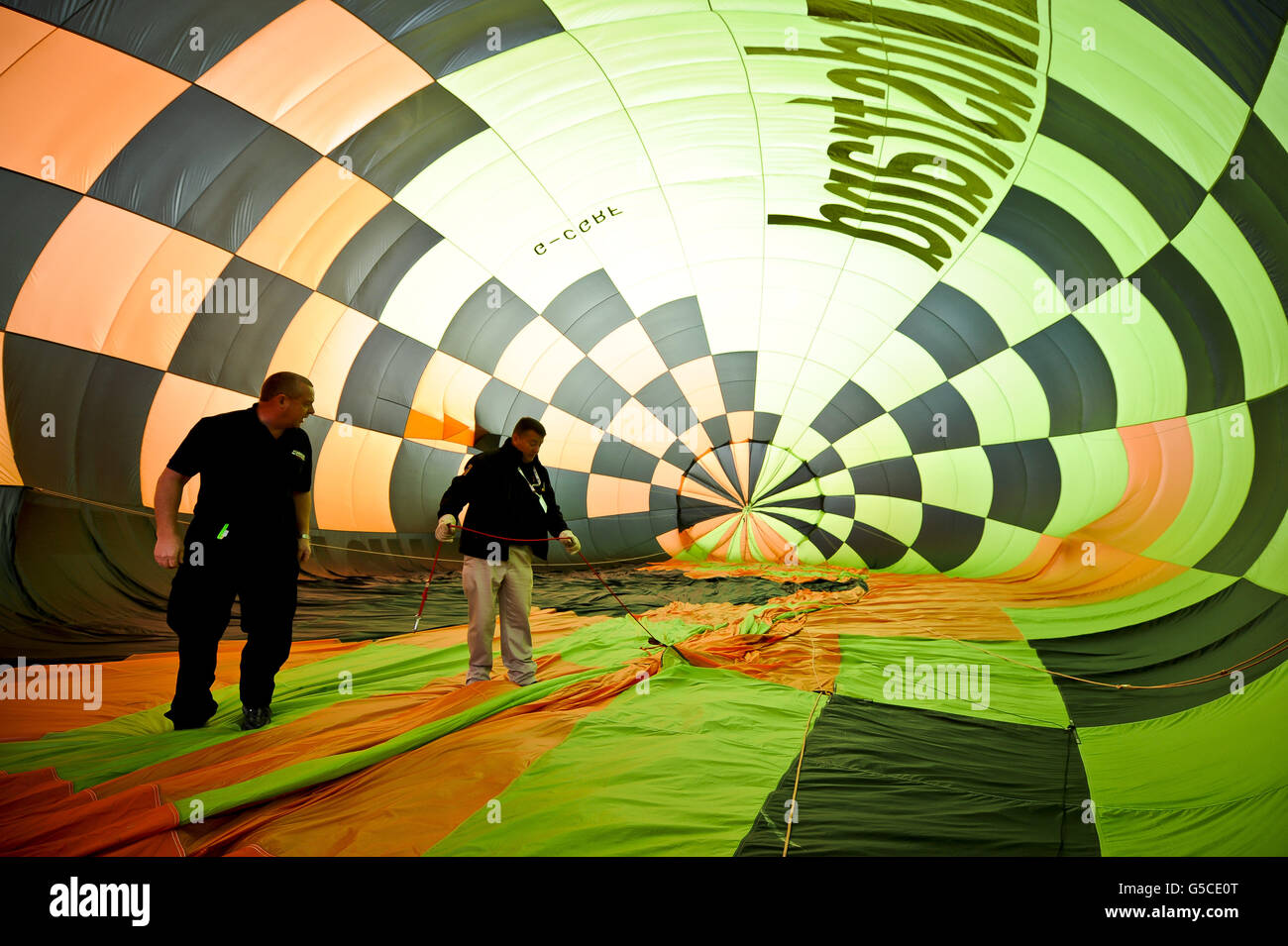 I mongolfiere controllano il rigging all'interno del suo pallone mentre una salita di massa si prepara a decollo alla 34a Fiesta Internazionale della mongolfiera di Bristol, Ashton Court Estate, mentre i mongolfiere provenienti da tutto il mondo si riuniscono in quello che è il più grande evento mongolfiera in Europa. Foto Stock