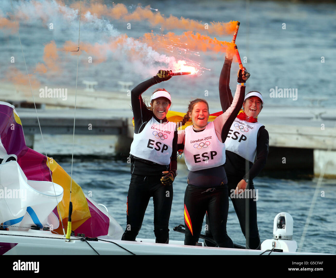 L'equipaggio spagnolo di gara olimpica (in tabardi bianchi) Tamara Echegoyen Dominguez, Sofia Toro Prieto Puga e Angela Pumariega Menendez celebrano la loro vittoria della medaglia d'oro sull'Australia nell'odierna finale di gara olimpica Elliott a Weymouth. Foto Stock