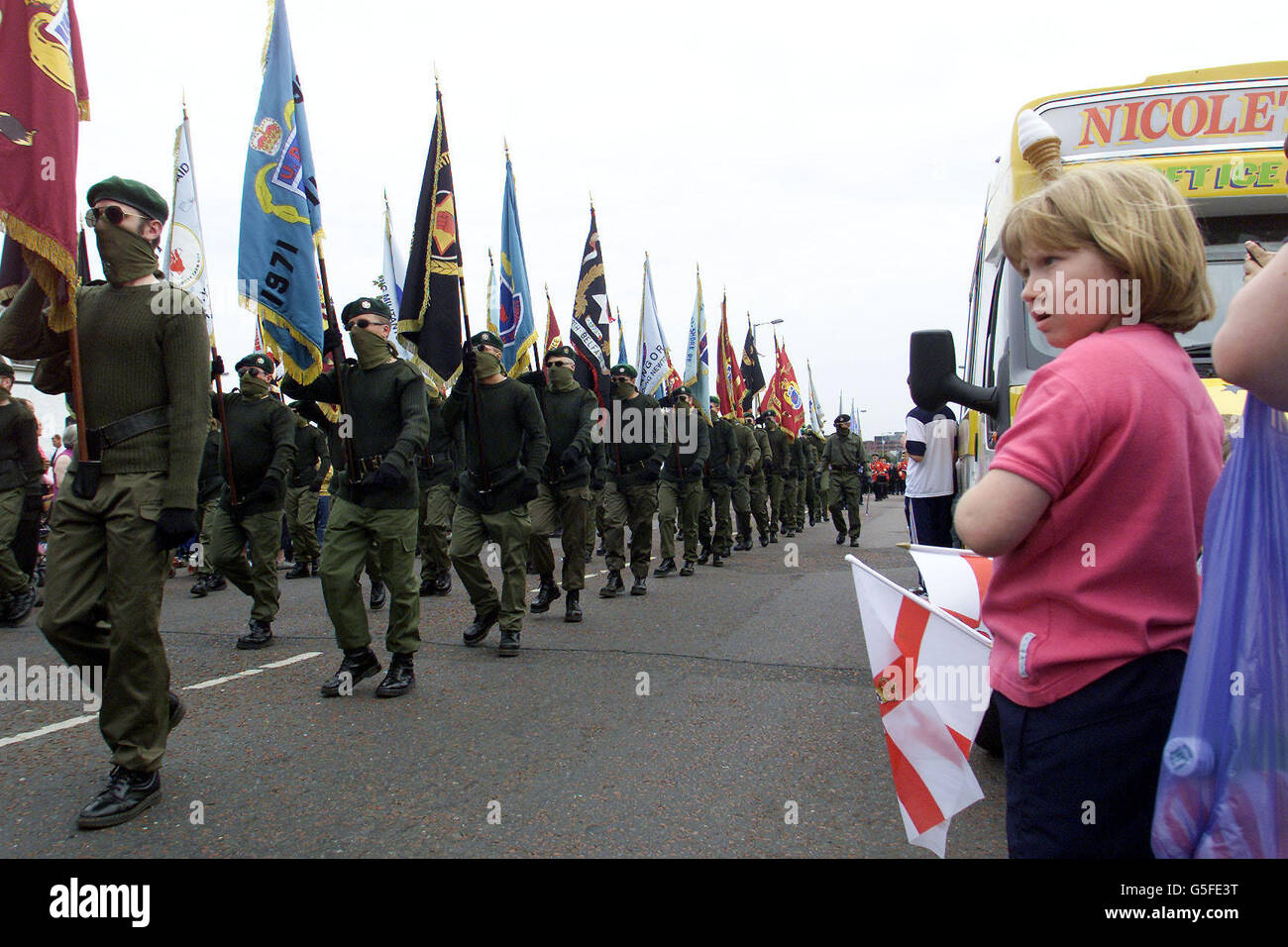 Una giovane ragazza guarda UFF mascherato (Ulster Freedom Fighters) uomini che marciano sulla Shankill Road per pagare il loro rispetto a Jackie Coulter della UFF. Coulter è stato ucciso l'anno scorso in un feudo Loyalist tra la UVF (Ulster Volonteer Force) e l'UFF. * migliaia di tifosi hanno marciato intorno all'area Shankill di Belfast prima di porre le corone al murale. Foto Stock