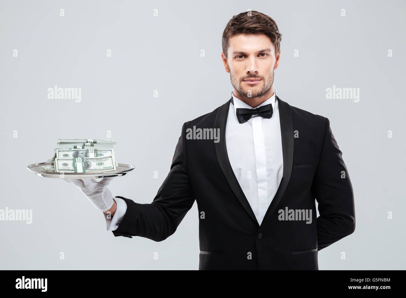 Bel giovane cameriere in smoking in piedi e tenere i soldi sul vassoio Foto Stock