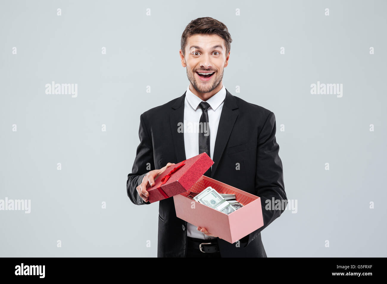 Felice eccitato giovane impreditore azienda confezione regalo pieno di denaro su sfondo bianco Foto Stock
