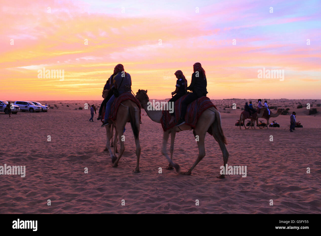 Turisti che si godono le corse di cammelli e del tramonto, safari nel deserto, Dubai, UAE Foto Stock