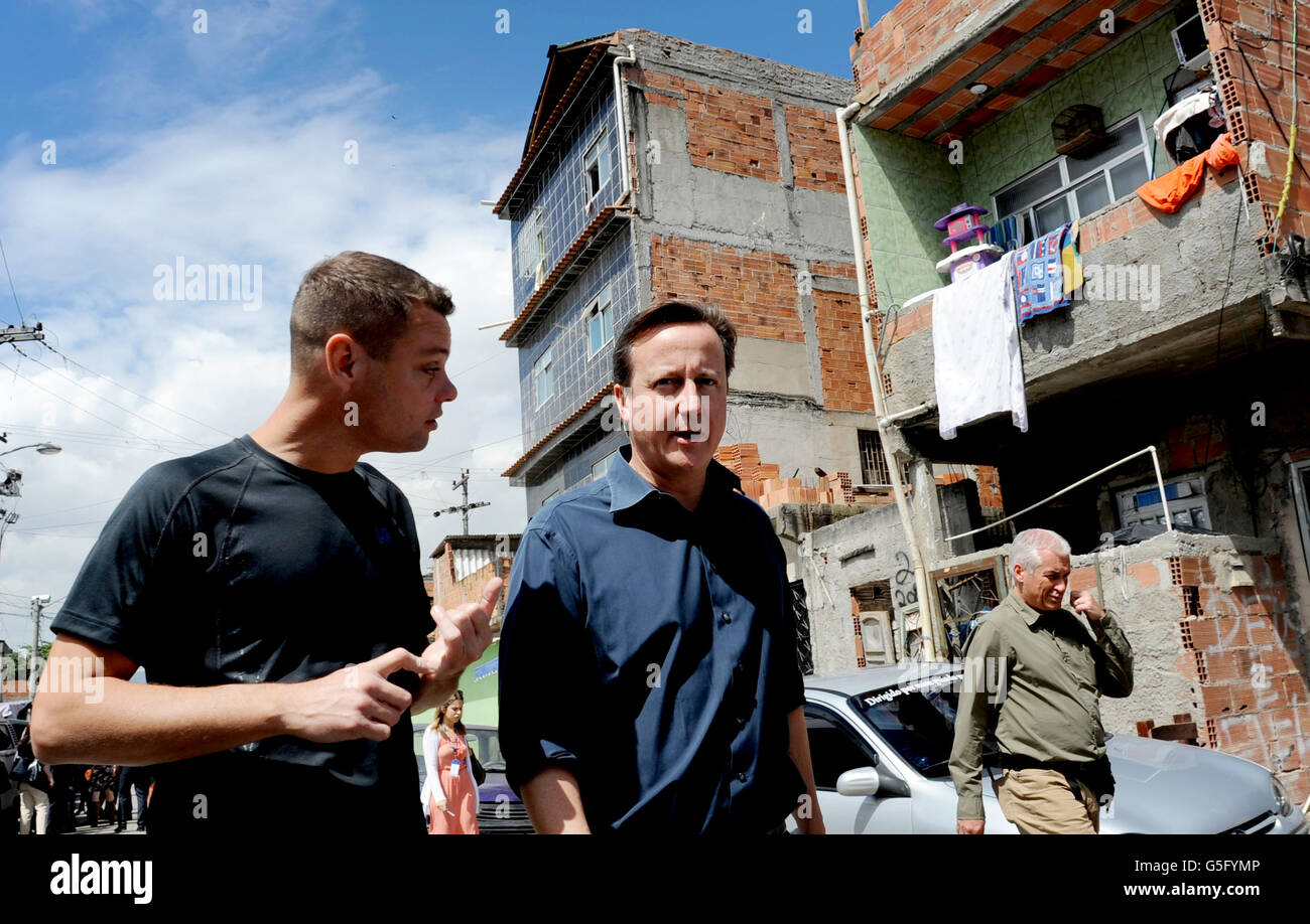 Il primo ministro David Cameron cammina oggi intorno a Mare Favela a nord di Rio De Janeiro, dove ha visto il progetto Luta Pela Paz che aiuta a allontanare i giovani da un crimine di vita e dalla droga e nello sport. Il direttore del progetto Luke Dowdney (a sinistra) ha mostrato al primo Ministro, che è in visita di due giorni in Brasile, intorno alla favela unpacified che non ha controllo della polizia. Foto Stock