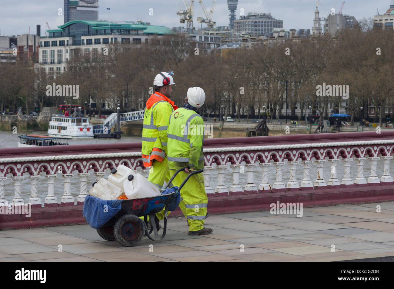 Due operai a elevata visibilità per capi di abbigliamento e copricapi rigidi attraversando un ponte sul fiume Tamigi a Londra, volti oscurati Foto Stock