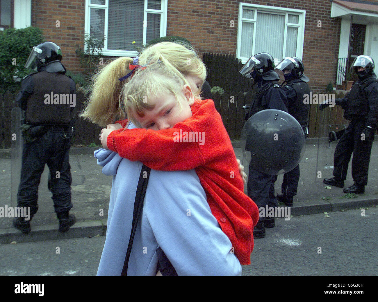 Un bambino cattolico è trasportato dalla madre, dietro gli schermi di sicurezza dell'esercito per essere portato alla scuola elementare di Holycross a Ardoyne, nel nord di Belfast. Dopo le manifestazioni tese e violente, il sesto giorno della protesta è scomparso senza incidenti, anche se ci sono timori che potrebbe scatenarsi. di nuovo * ... I colloqui ritardati riprendono tra i residenti lealisti e il Segretario di Stato John Reid. Foto Stock