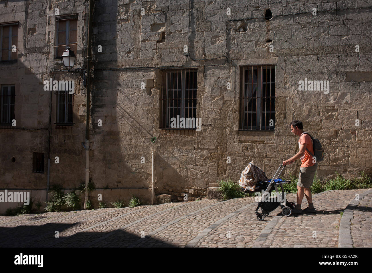 Padre spinge il bambino attraverso la mattina presto luce sulle pareti di architettura off Place de la Canourge nella vecchia Montpellier, Francia Foto Stock